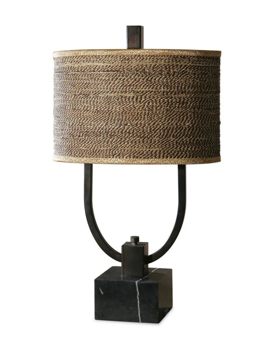 Rustic table lamp with burnished bronze body, black marble base, and a woven rattan oval drum shade with decorative trim.